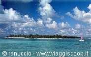 Coral island with sailboat amid turquoise sea and white clouds