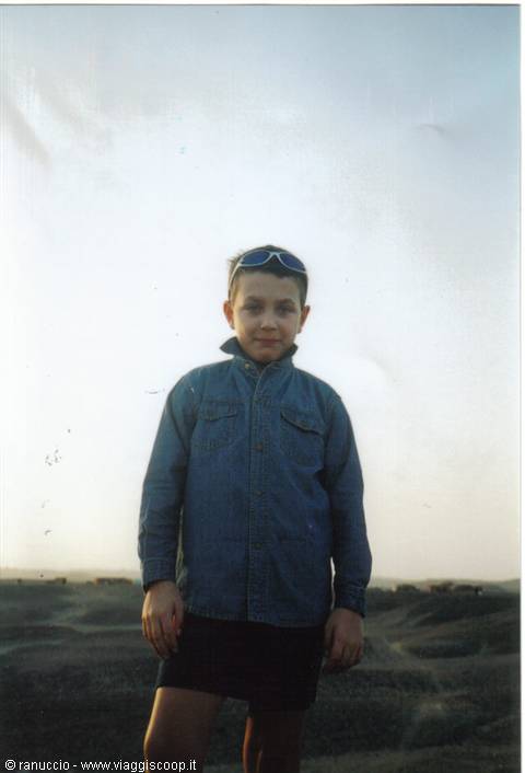 Boy in denim shirt with sunglasses on his head, standing on arid hills