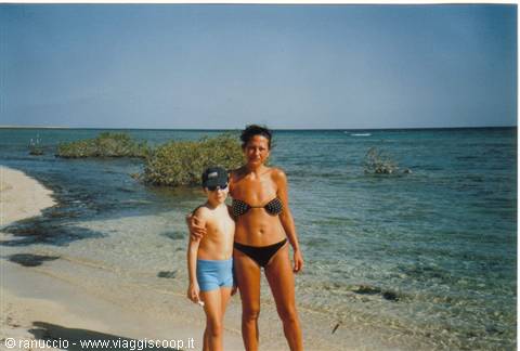Woman in bikini and boy in cap on beach by turquoise sea