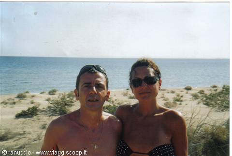 Man and woman in swimwear wearing sunglasses on sandy beach by the sea