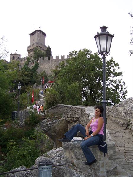 Woman sitting on a stone wall, Guaita tower in San Marino behind