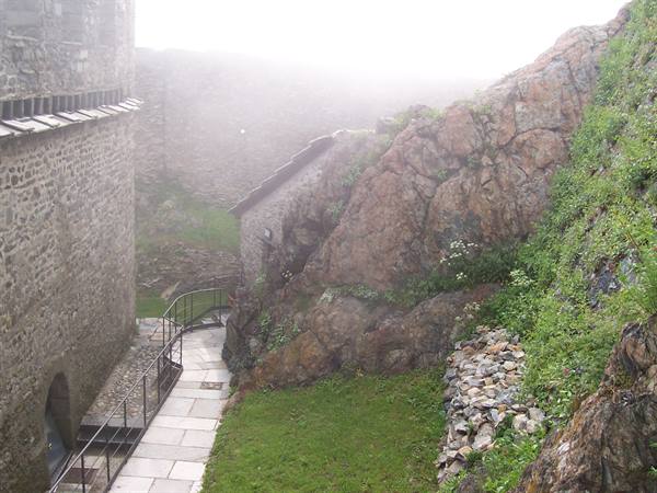 Stone-paved path between fortress walls and mossy rock in thick fog
