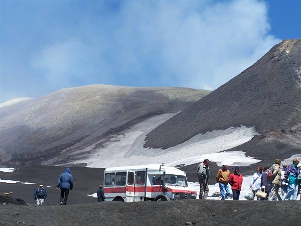 Tourists and pink bus among volcanic craters and snow, likely Mount Etna