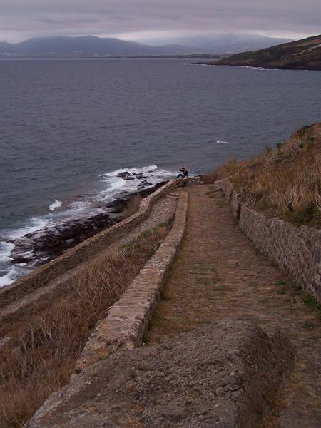Stone-paved path along the cliff, a person photographs the sea