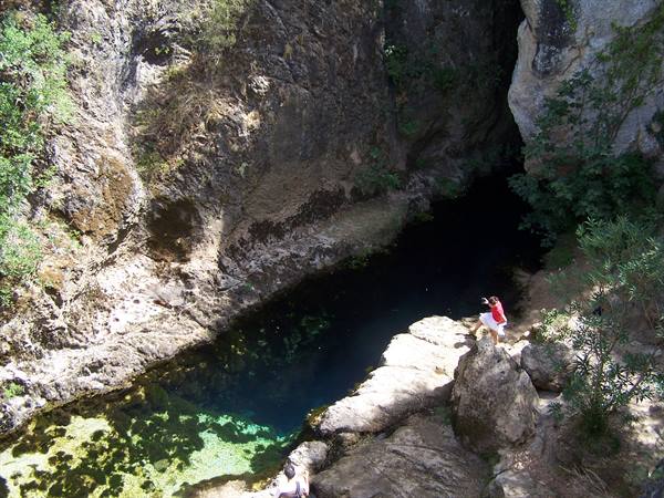 Tourist in red standing on limestone rocks beside an emerald natural swimming pool