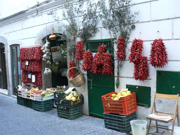 Red chili peppers hanging on white facade, crates of fruit outside the shop