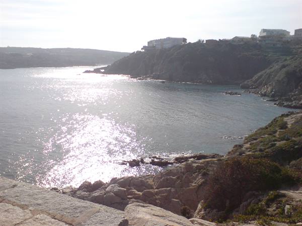 Sunlight glinting on the sea among granite rocks and houses on the cliff, Santa Teresa di Gallura