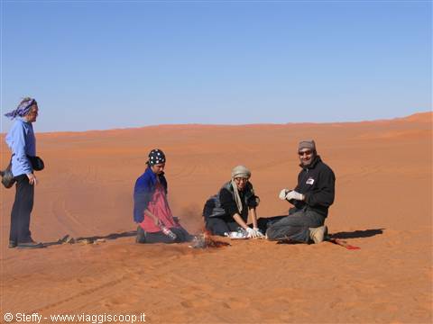 Travelers crouching on red sand among desert dunes