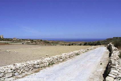 White dirt road between dry stone walls, plowed fields and blue sea ahead