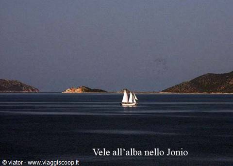 Two-sailed wooden boat on calm sea between dark hills at dawn