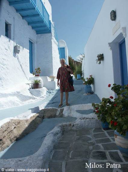 Woman walks the stone lane of Milos Patra among whitewashed houses and geraniums