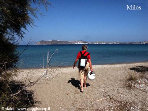 Tourist carrying a helmet walks toward the sea in Milos