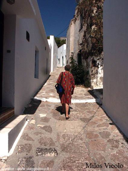 Woman in red dress walks the stone-paved alley of Milos between whitewashed houses