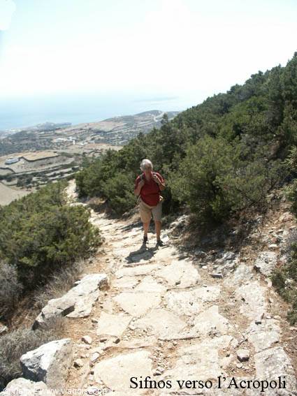 Sifnos, toward the acropolis: hiker on a stone path among shrubs, sea in the distance