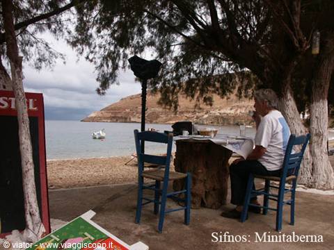 Sifnos, Minitaberna: shaded tavern table on the beach with a boat offshore