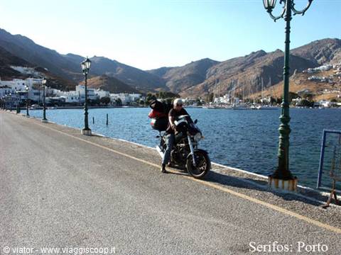 Loaded motorcyclist riding along Serifos port pier, green iron lampposts