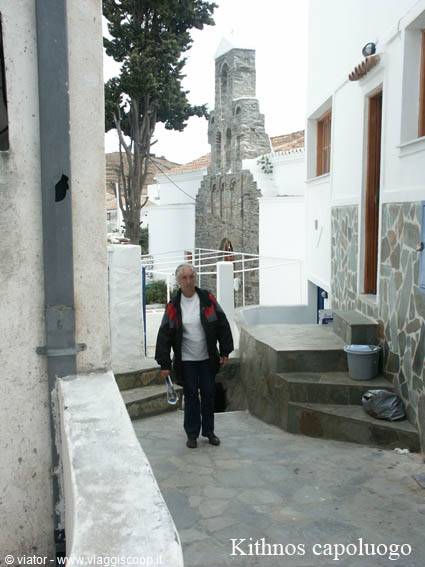 Man carrying bag on steps among white houses and stone church in Chora, Kithnos