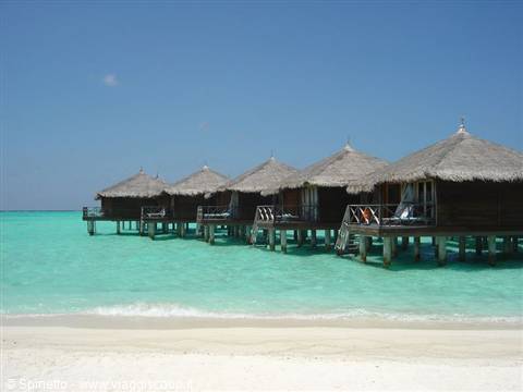 Thatched overwater bungalows on stilts above turquoise water, white sandy beach