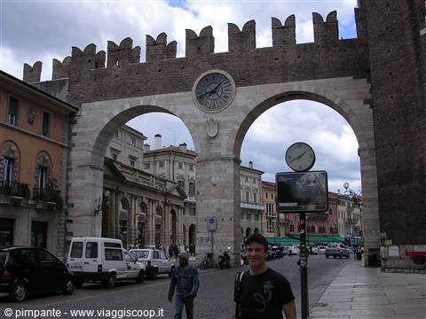 Traveler under Verona's Bra gates, crenellated walls and clock above