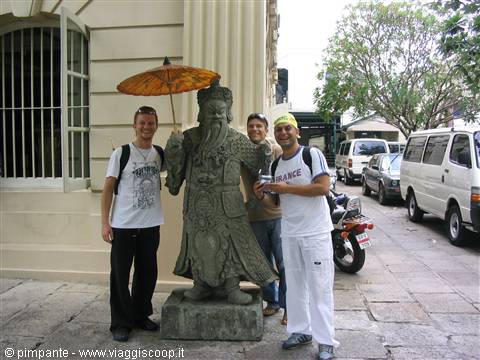 Tourists beside a warrior statue holding an umbrella, street with white vans