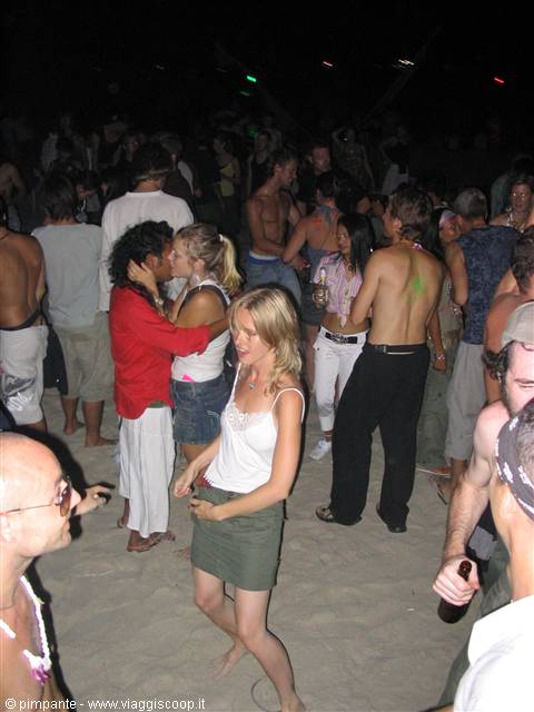 Night beach party, crowd dancing barefoot on the sand