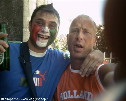 Italian fan with tricolor face paint and beer hugs friend in orange Holland shirt