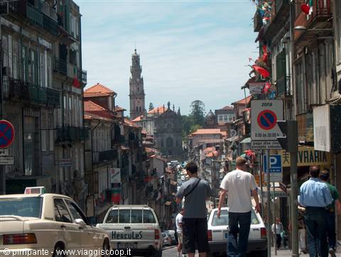 Pedestrians and cars descend a steep street with the Clérigos Tower behind