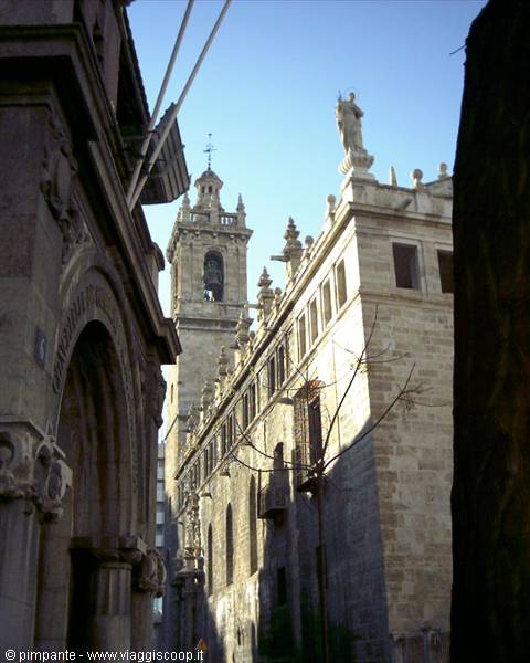 Stone church with bell tower and statues between buildings, sunlight