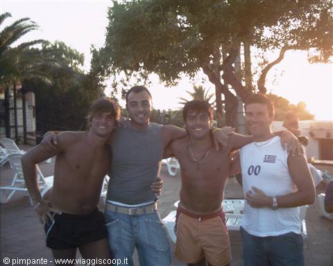 Four friends in summer clothes embrace under a palm tree in the sun