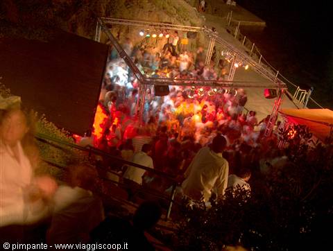 Crowd dancing at night under colorful stage lights near the sea
