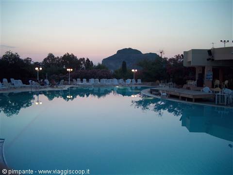 Empty pool with white loungers and lit lamppost, dark mountain in twilight background