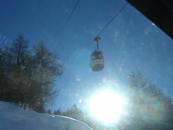 Cable car cabin above snow between firs, bright sun and blue sky