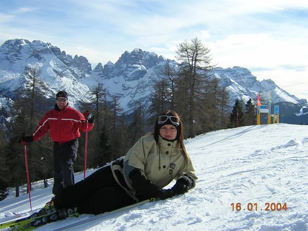 Two skiers on the snow with snowy Dolomites peaks and larches behind