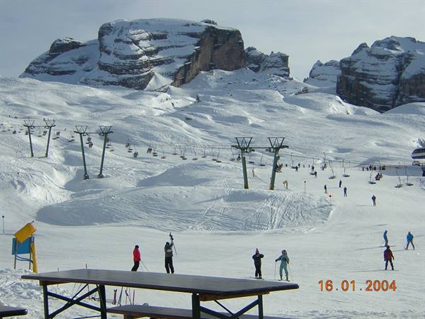 Skiers on snow with chairlift and Dolomite peaks in background