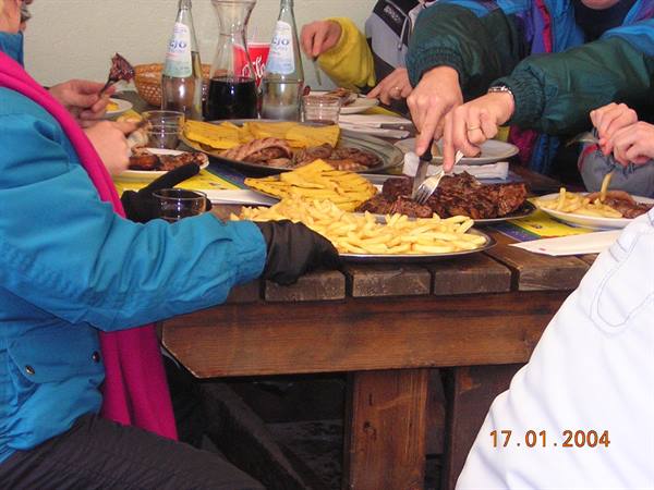 People eating grilled meat and fries at a wooden table