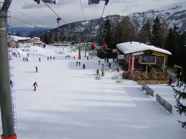 Skiers on the snow beneath the chairlift, snowy wooden mountain hut among larches