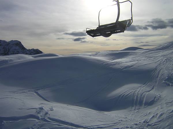 Empty chairlift backlit above snowy slopes with ski tracks