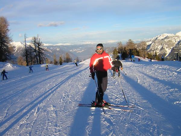 Skier in red jacket pausing on snowy slope, mountains and larches behind