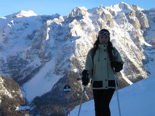 Skier in beige jacket with poles in front of snow-covered peaks, blue sky