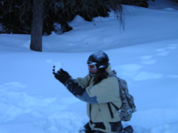 Girl in helmet and backpack taking a photo in deep snow among trees