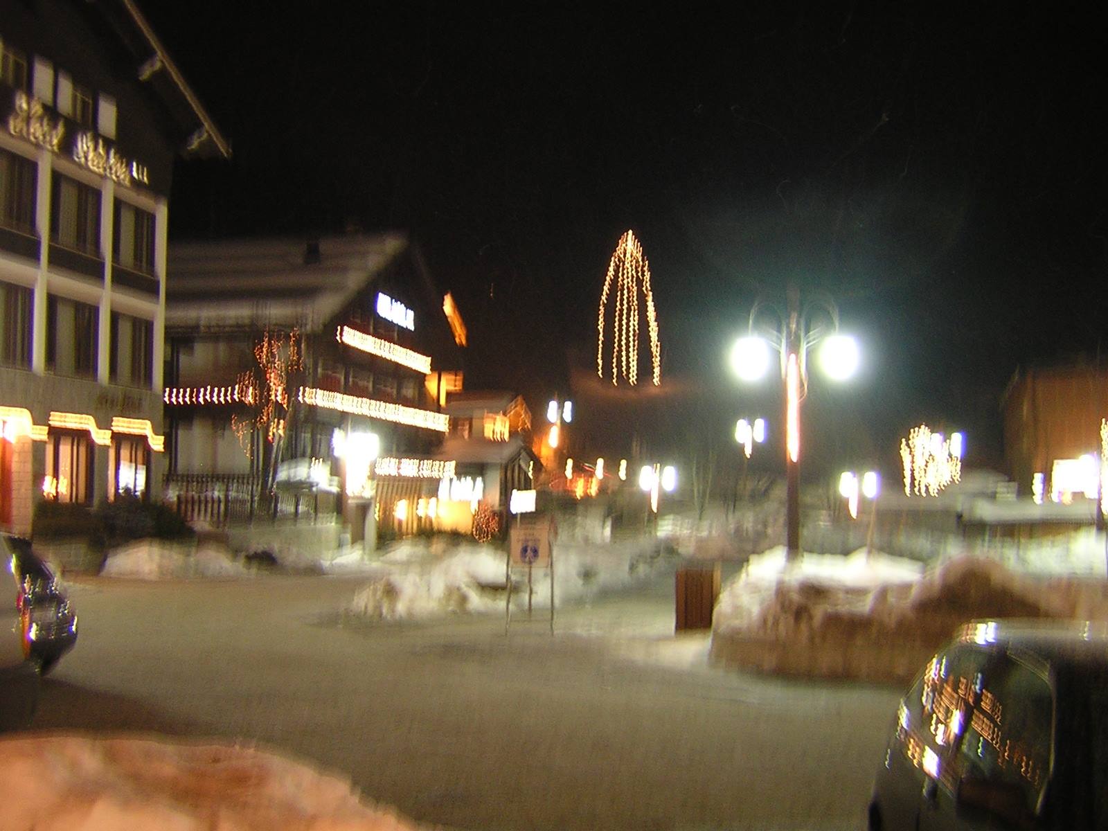 Snowy square at night with glowing chalets and lit Christmas tree