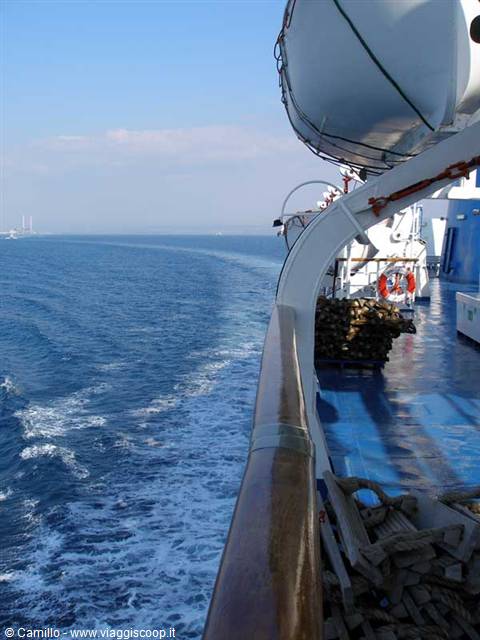 Ferry underway: white wake on blue sea, wooden railing and lifeboats