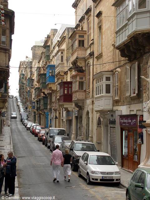 Steep street with traditional wooden balconies, parked cars and pedestrians, Valletta