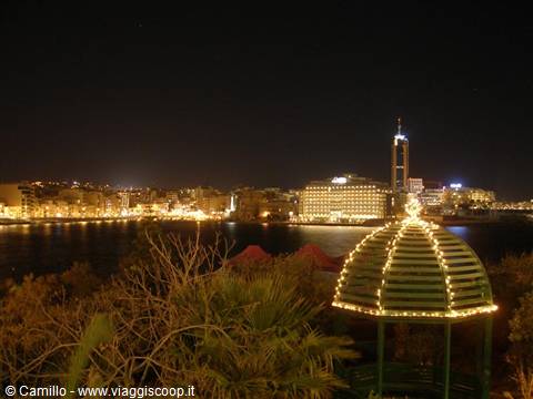 Lit gazebo in front of Sliema's night harbor, yellow lights on buildings