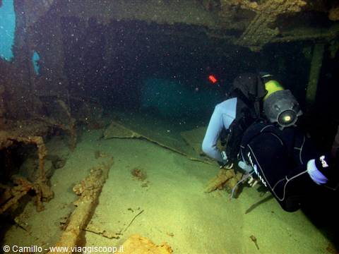 Diver with flashlight explores inside a sunken shipwreck