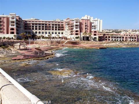Large pink hotel by the rocky shore, clear waves and blue sky