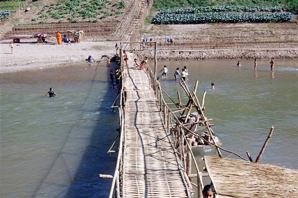 Bamboo bridge across the river, people crossing and swimming nearby