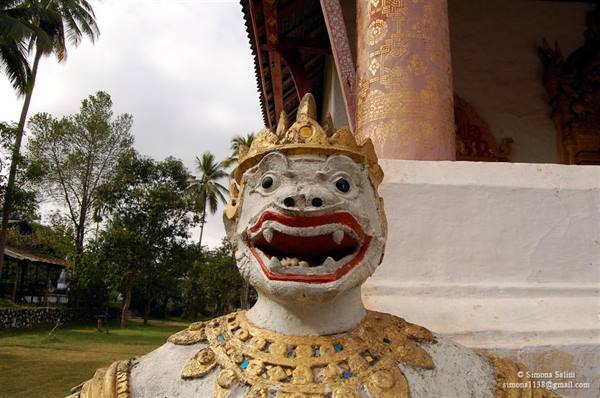 Guardian statue with golden crown in front of a Buddhist temple among palm trees