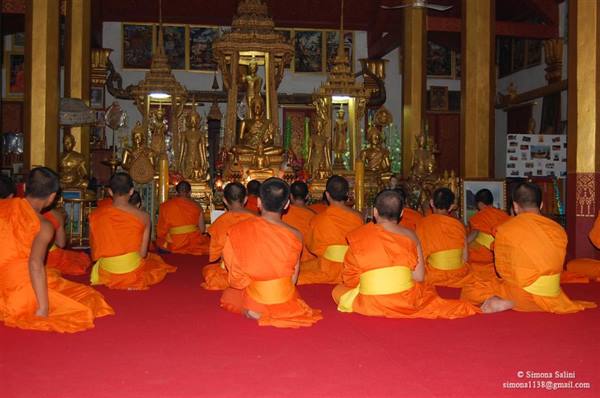 Monks in orange robes praying seated before golden Buddha statues in temple