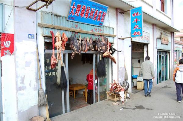 Butcher shop with hanging meat outside, Chinese signboards, pedestrians walking by